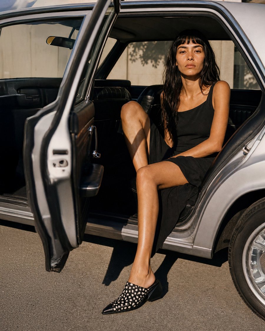 Model in black dress and polka-dot mules, exiting car